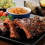 Racks of barbecue ribs drenched in sauce wiht salad and cornbread